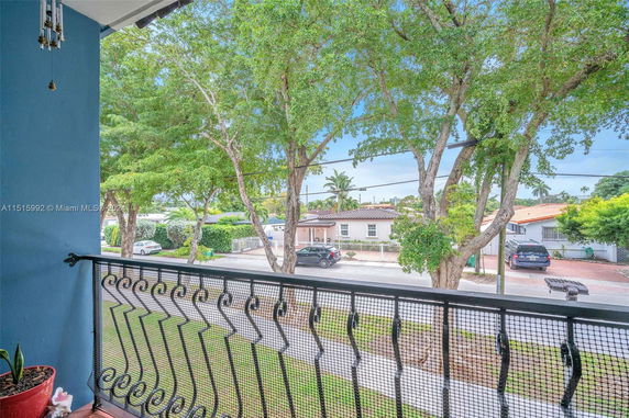 View from a balcony overlooking a residential street with trees and houses.