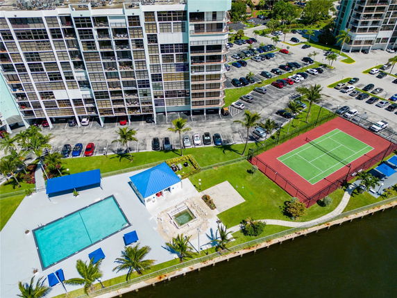 Aerial view of a parking area, tennis court, swimming pool, and waterfront.