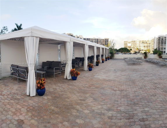 Rooftop area with seating under canopies and potted plants, surrounded by buildings.
