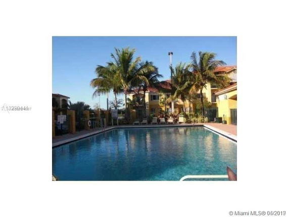 View of a swimming pool surrounded by palm trees and a building in the background.