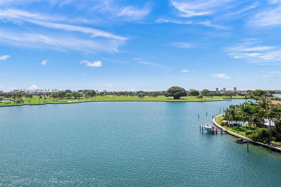 Wide view of a large body of water with green land and trees in the background under a blue sky.