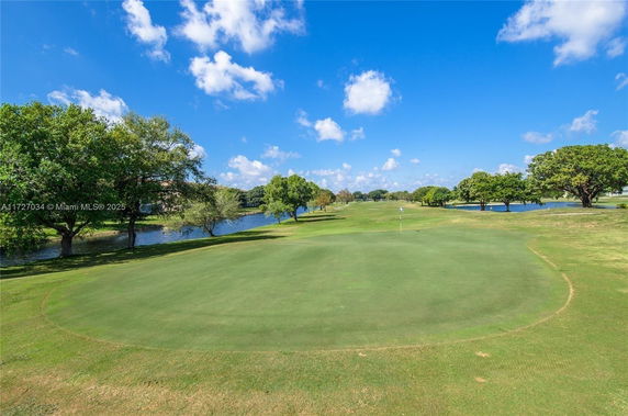 Open view of a golf course with a green area and trees.