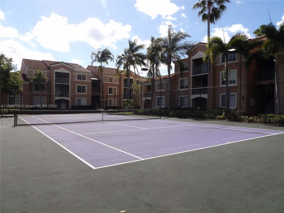 Tennis court in front of multi-story apartment buildings with palm trees nearby.