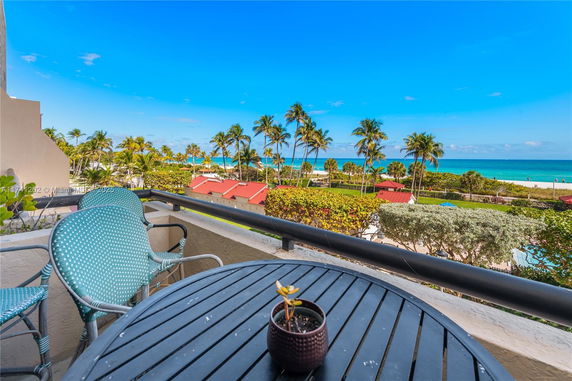 View from a balcony overlooking a beach with palm trees and ocean.