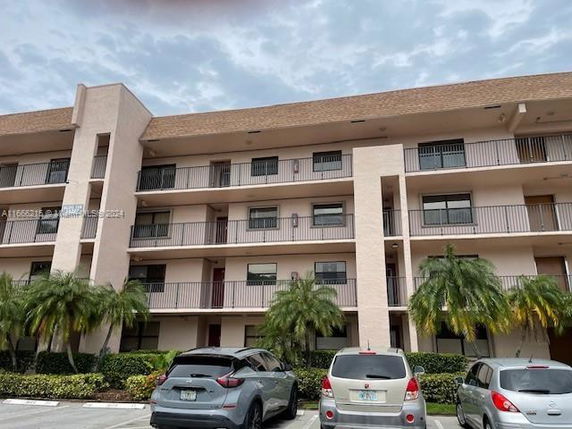 Front view of a multi-story apartment building with balconies and parking area in front.