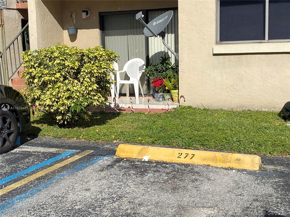 Outdoor parking space numbered 277 in front of a building entrance with a satellite dish, potted plants, and a chair.