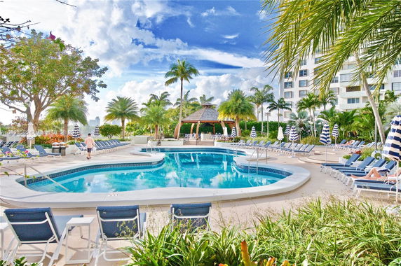 Outdoor pool area with lounge chairs and palm trees near a multi-story building.