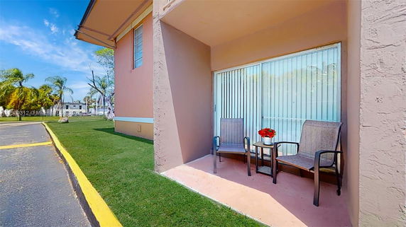 Side view of a building with a small patio area featuring two chairs and a table with potted flowers.