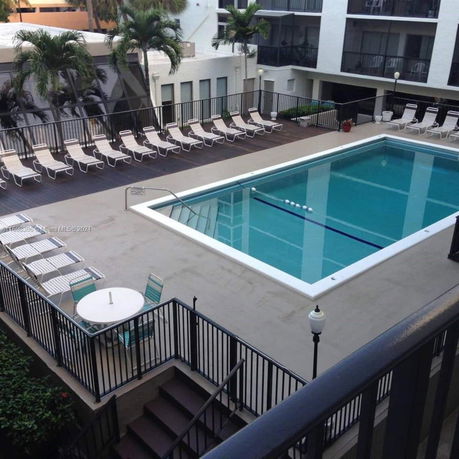 View of a swimming pool area surrounded by railing and deck chairs, adjacent to a multi-story building.
