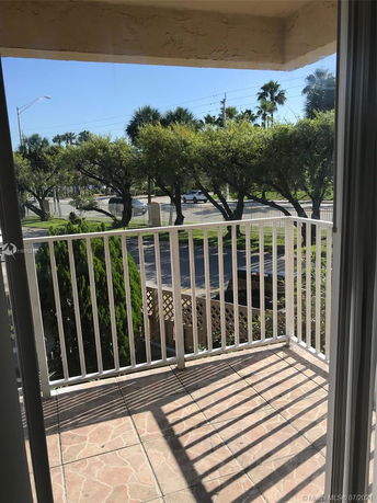 View from a balcony with a railing, showing trees and a road in the background.