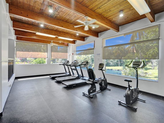 Gym area with treadmills and stationary bikes, featuring large windows and wooden ceiling beams.