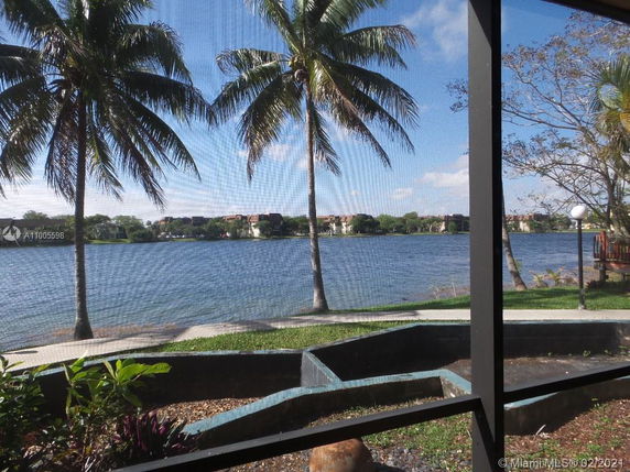 View of a lake with palm trees and residential buildings in the distance.
