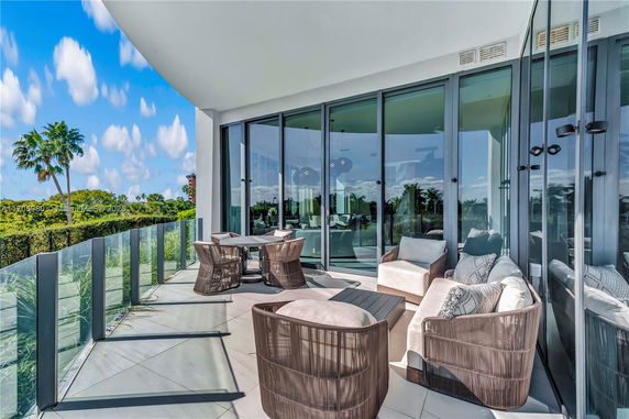 Outdoor patio area with glass railing and outdoor furniture, offering a panoramic view with palm trees in the background.
