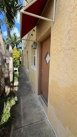 Side view of a building showing a narrow pathway with an entrance door and a red awning.