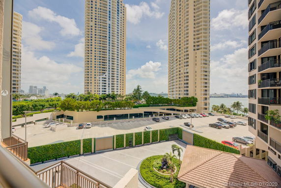 View of tall residential buildings with a parking area and distant cityscape.