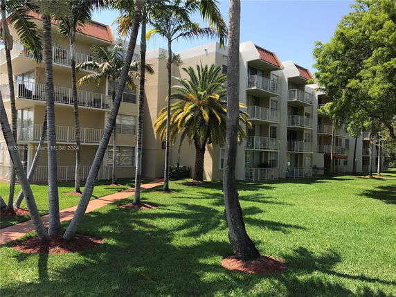Front view of a multi-story apartment building with balconies and surrounding palm trees.