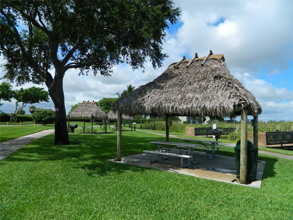 Outdoor area with picnic tables under thatched shelters and greenery.