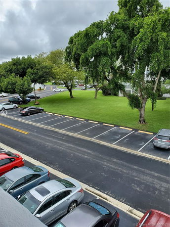Outdoor parking area with multiple cars and a nearby grassy area with trees.