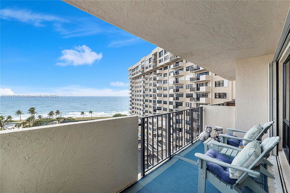 Balcony view overlooking a beach and ocean with a nearby apartment building.