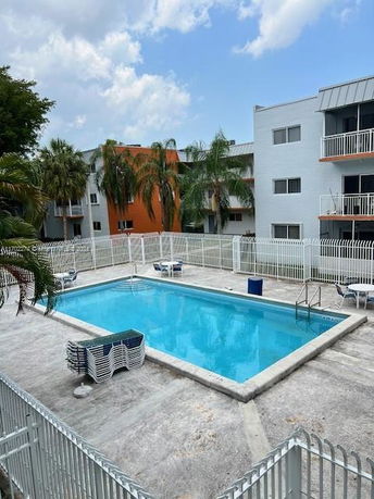 Outdoor swimming pool surrounded by a white fence near an apartment building.