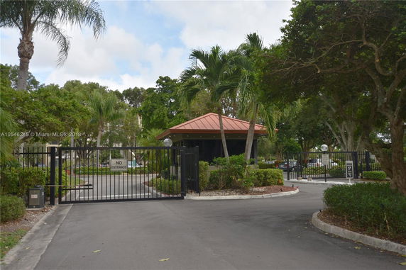 Front view of a gated entrance with a small guardhouse and surrounding vegetation.