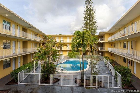 View of a three-story apartment building surrounding a central outdoor swimming pool.