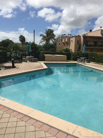 Outdoor swimming pool area with clear water, surrounded by a tiled deck and landscaping.