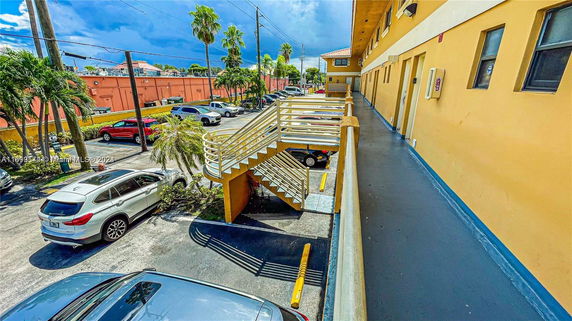 Outdoor parking area with several cars parked and a yellow building beside it.