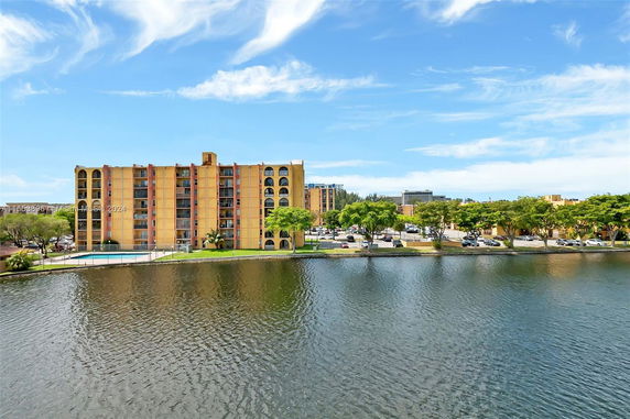 View of a multi-story building next to a body of water with adjacent parking area.