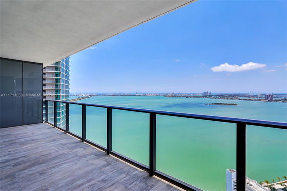 Panoramic view from a high-rise balcony overlooking the ocean and city skyline.