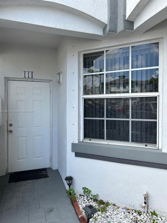 Entrance of a house with a white door and a large window beside it.