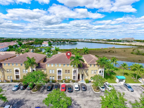 Aerial view of two-story residential buildings with a parking area in front and a scenic landscape with water bodies and greenery in the background.