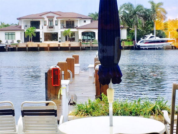 Two-story house with a brown tile roof by the water, featuring balconies and multiple large windows.