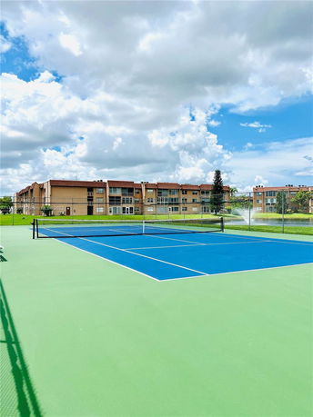 View of a blue and green tennis court with buildings in the background.