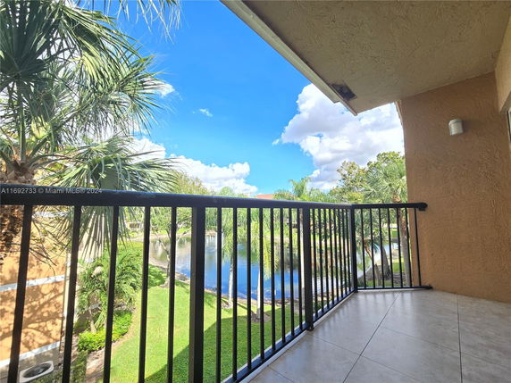 Balcony view overlooking a pond with trees and a bright blue sky.