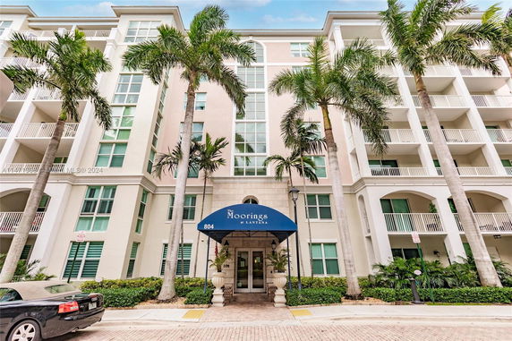 Front view of a multi-story residential building with balconies and palm trees.