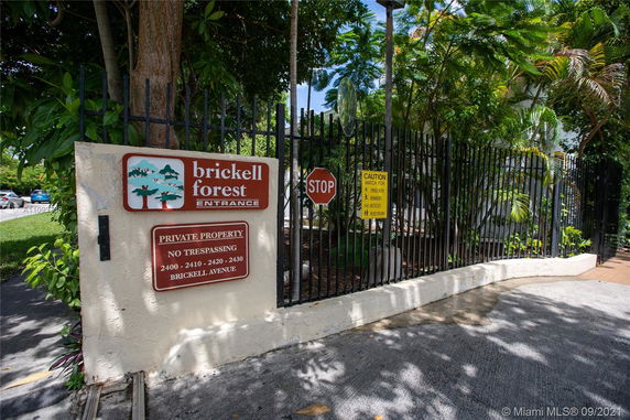 Entrance view of Brickell Forest private property with signage and gated fence.