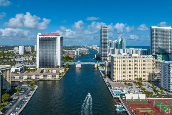 Wide angle view of a coastal cityscape with high-rise buildings, waterway, and bridge.