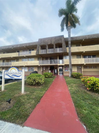 Front view of a three-story building with balconies and a red pathway leading to the entrance.
