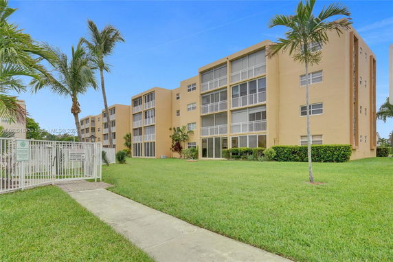 Front view of a multi-story apartment building with balconies and palm trees.