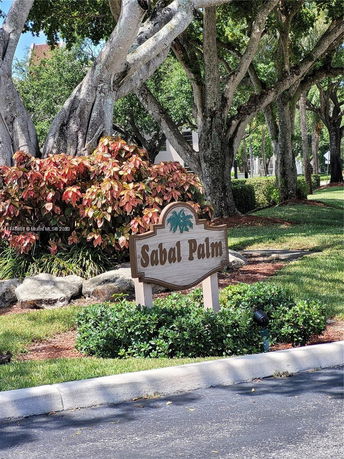 Signage for Sabal Palm surrounded by trees and plants.