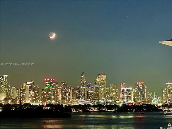 Night view of a city skyline with a crescent moon above.