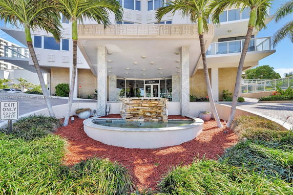 Front view of a building entrance with a fountain and palm trees.