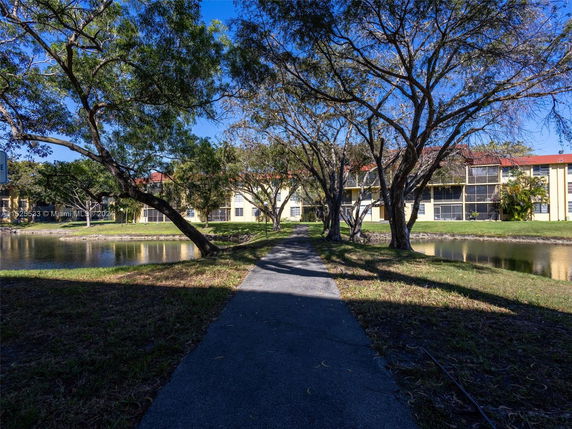 View of a building with multiple units seen through trees and across a pond.
