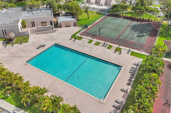 Aerial view of a swimming pool adjacent to sports courts and a building.