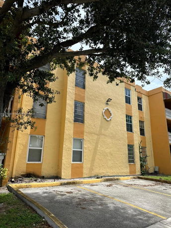 Front view of a multi-story residential building with yellow exterior and parking area.