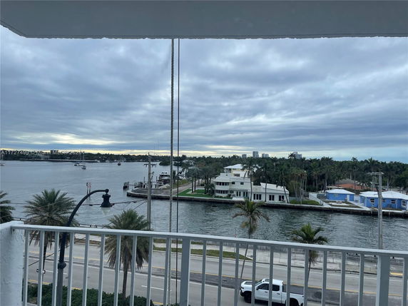 View from a balcony overlooking a waterway with houses and greenery in the distance.