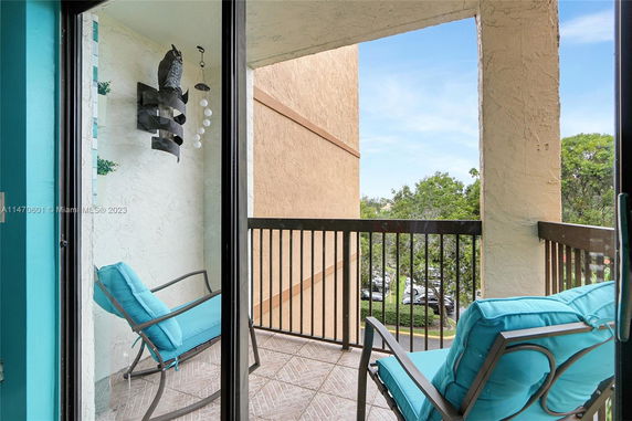 View from a balcony with two chairs and decorations, overlooking trees and a parking lot.
