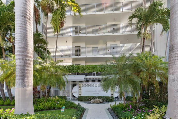 Front view of a multi-story residential building with balconies and surrounded by palm trees.
