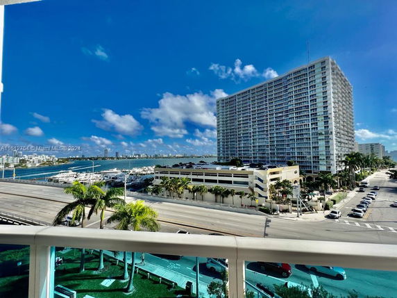 Panoramic view of a large modern building near a waterfront, with a marina and cityscape in the background.